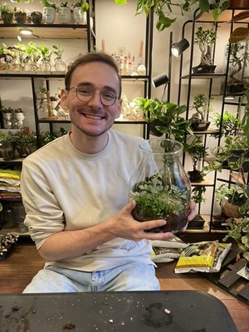 Ryan holding a newly made terrarium among shelves of houseplants